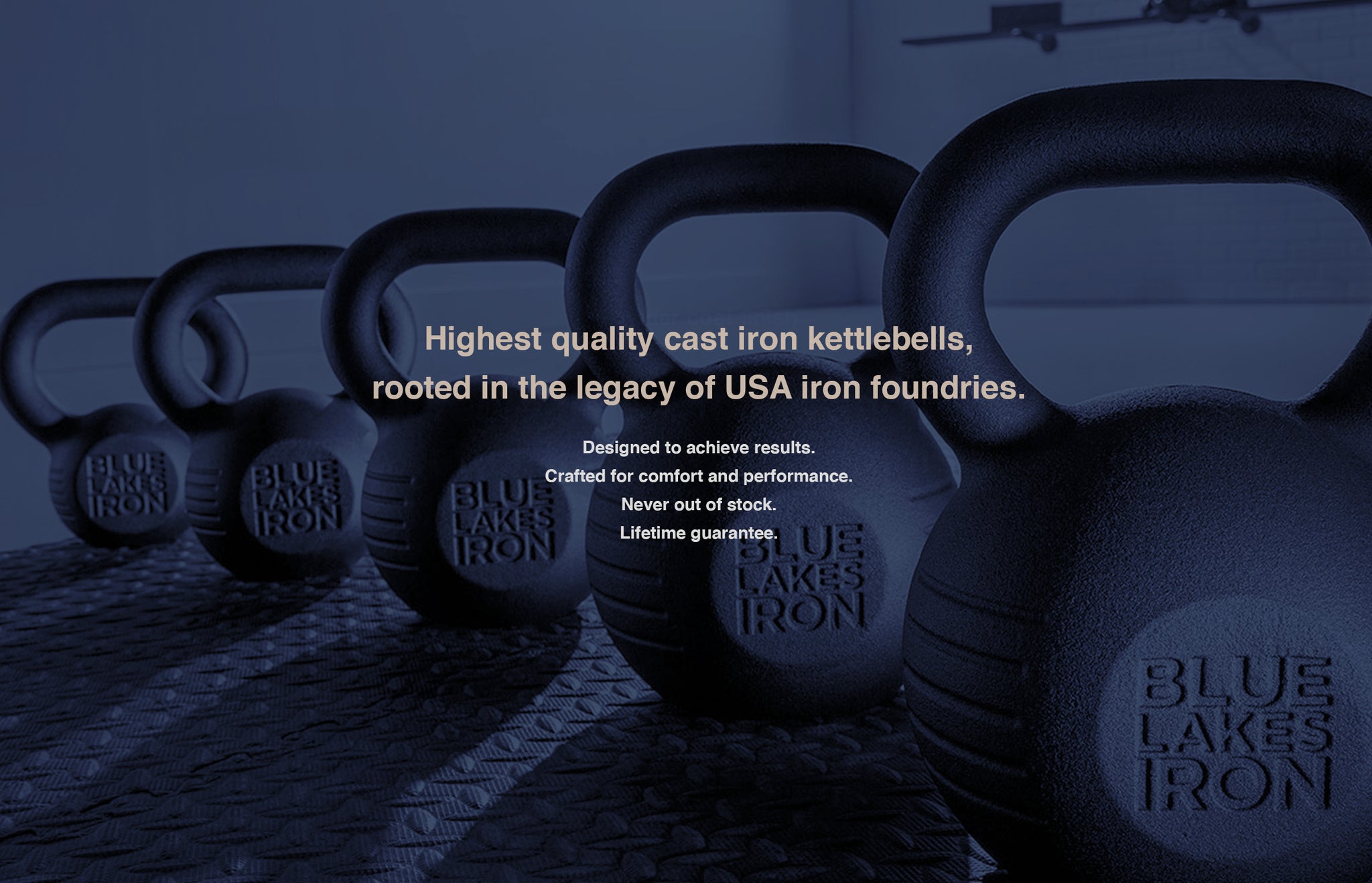 Blue Lakes Iron kettlebells in different weight increments are lined up in a diagonal row in a dark fitness gym.