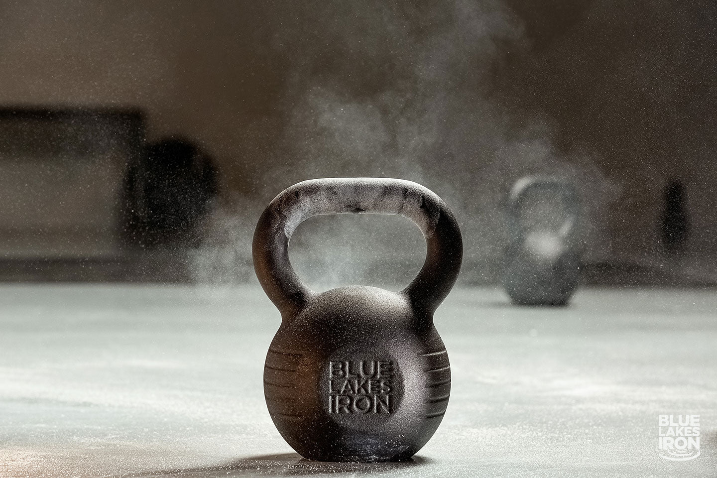 cast iron kettlebell made by Blue Lakes Iron sits on a gym floor. Weightlifting chalk dust is in the air.