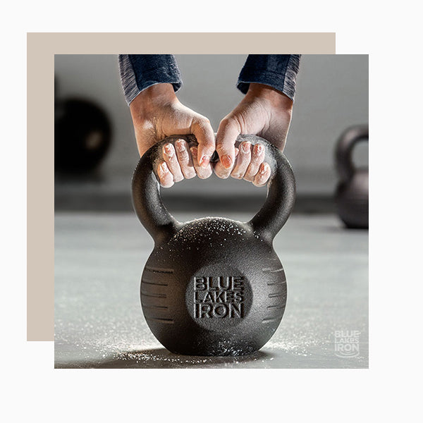 Two hands covered with gym chalk grasp the wide handle opening of a kettlebell weight.