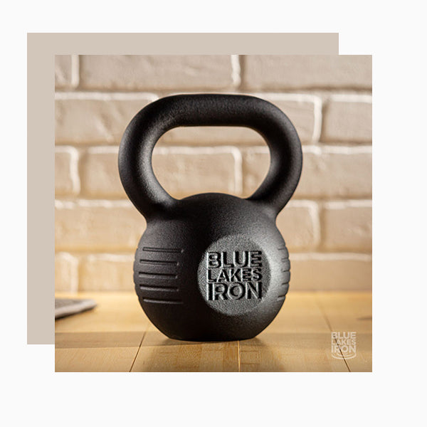 A powder coated kettlebell made by Blue Lakes iron sits on a table in front of a white brick wall.